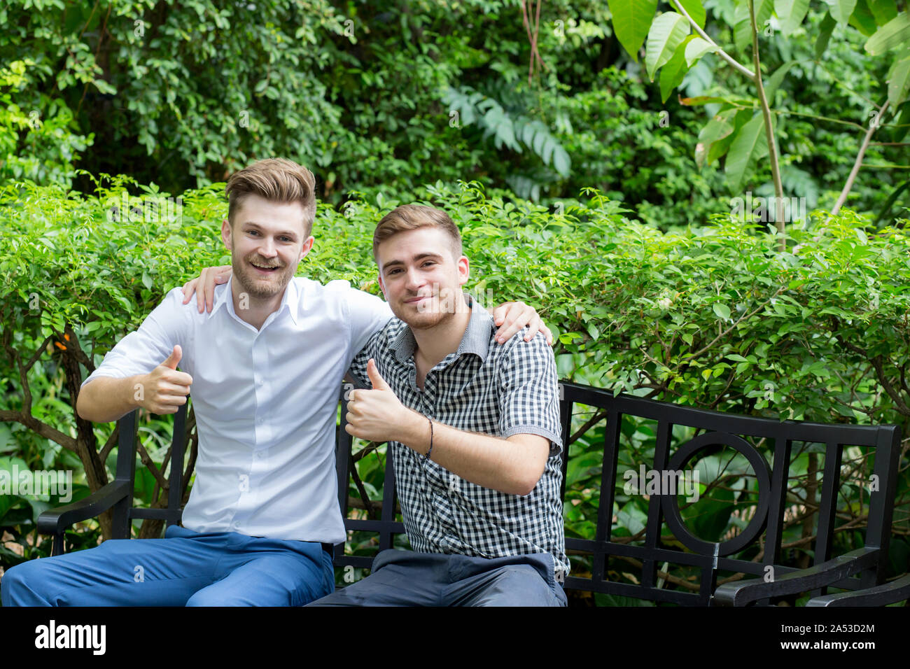 Due giovani felici uomini casual rendendo l'ok Thumbs up gesto a mano in giardino. Foto Stock