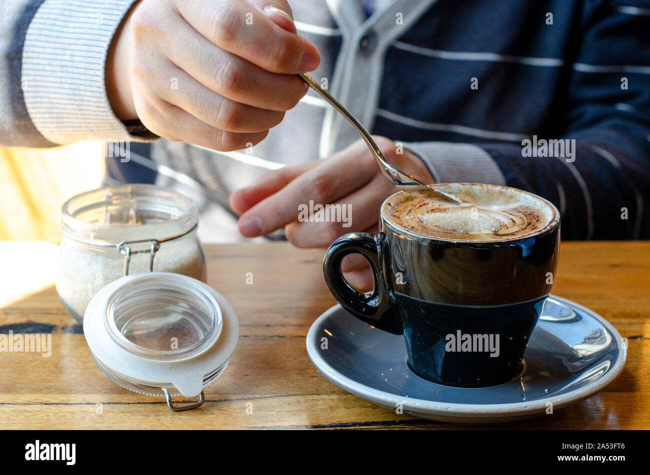 Uomo che versa lo zucchero da un contenitore nel suo caffè. Foto Stock