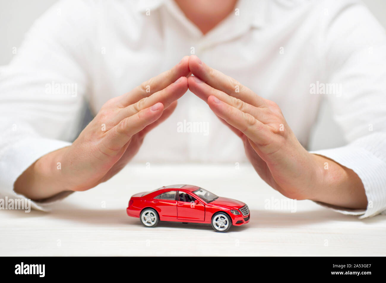 Protezione auto. Piccolo rosso auto coperti da mani di uomo. Auto (automobile) assicurazione e la rinuncia a danni da collisione concetti. Foto Stock