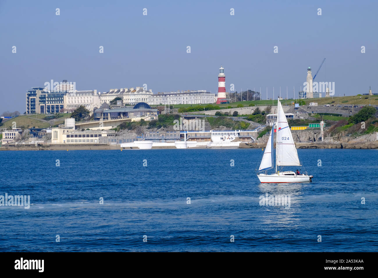 Un bianco yacht vele in Plymouth Sound passando la mitica Plymouth Hoe. Foto Stock