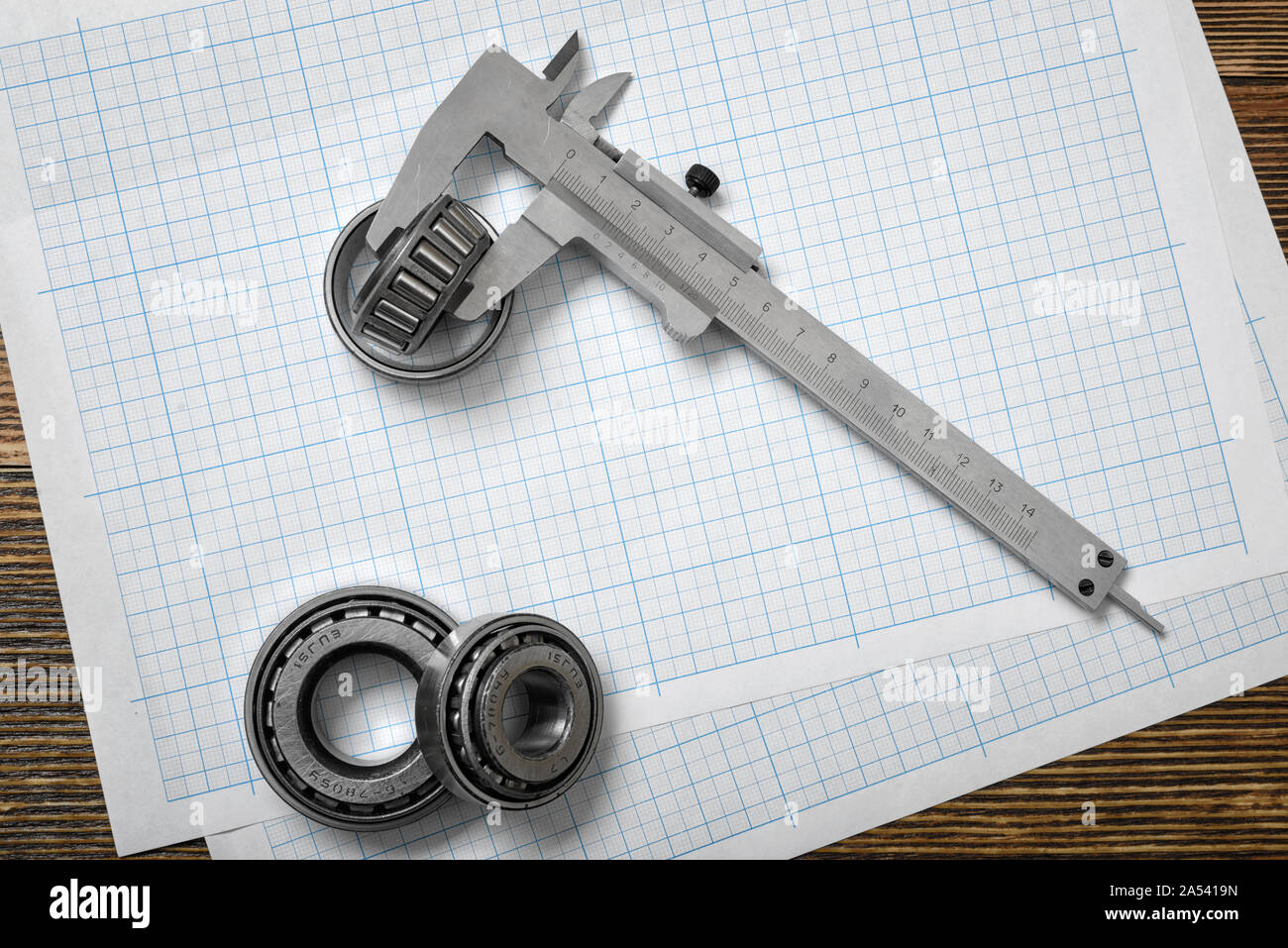 Una grande scala vernier giacente sulla sezione trasversale della carta con tre cuscinetti intorno ad esso su sfondo di legno. Foto Stock
