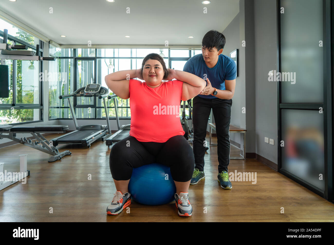 Due Asian trainer uomo e donna sovrappeso esercizio con sfera insieme in una palestra moderna, felice e sorridere durante gli allenamenti. Grasso donne prendersi cura della salute Foto Stock