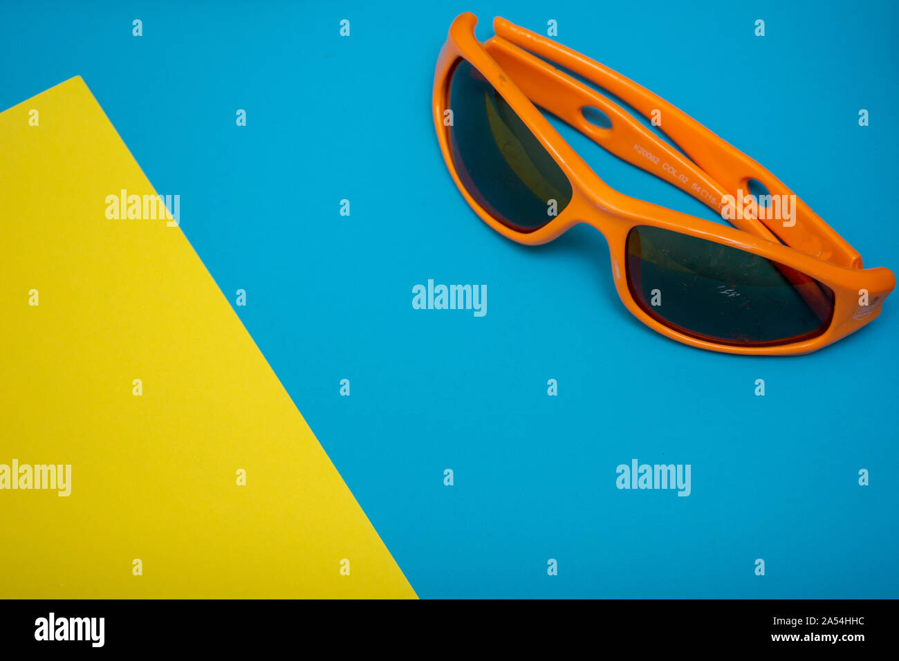 Occhiali da sole arancione su un luminoso blu e giallo piatto sfondo laici design con copia spazio. Pronto per il divertimento estivo. Foto Stock