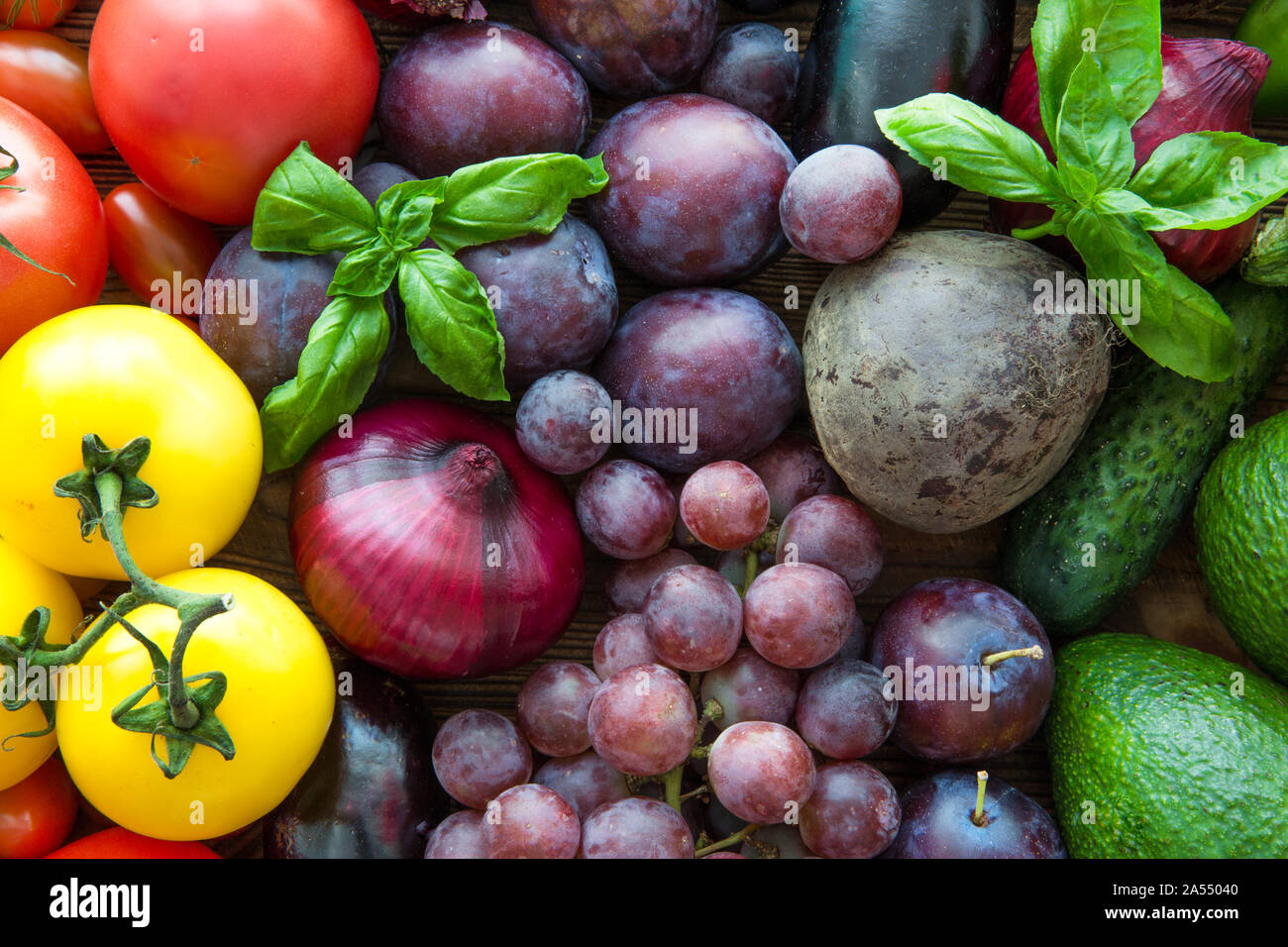 Diversi tipi di frutta e verdura, vista dall'alto. Violetto brillante uve,  prugne, colorato di verde avocado e le foglie di basilico. Pomodori di  colore giallo Foto stock - Alamy