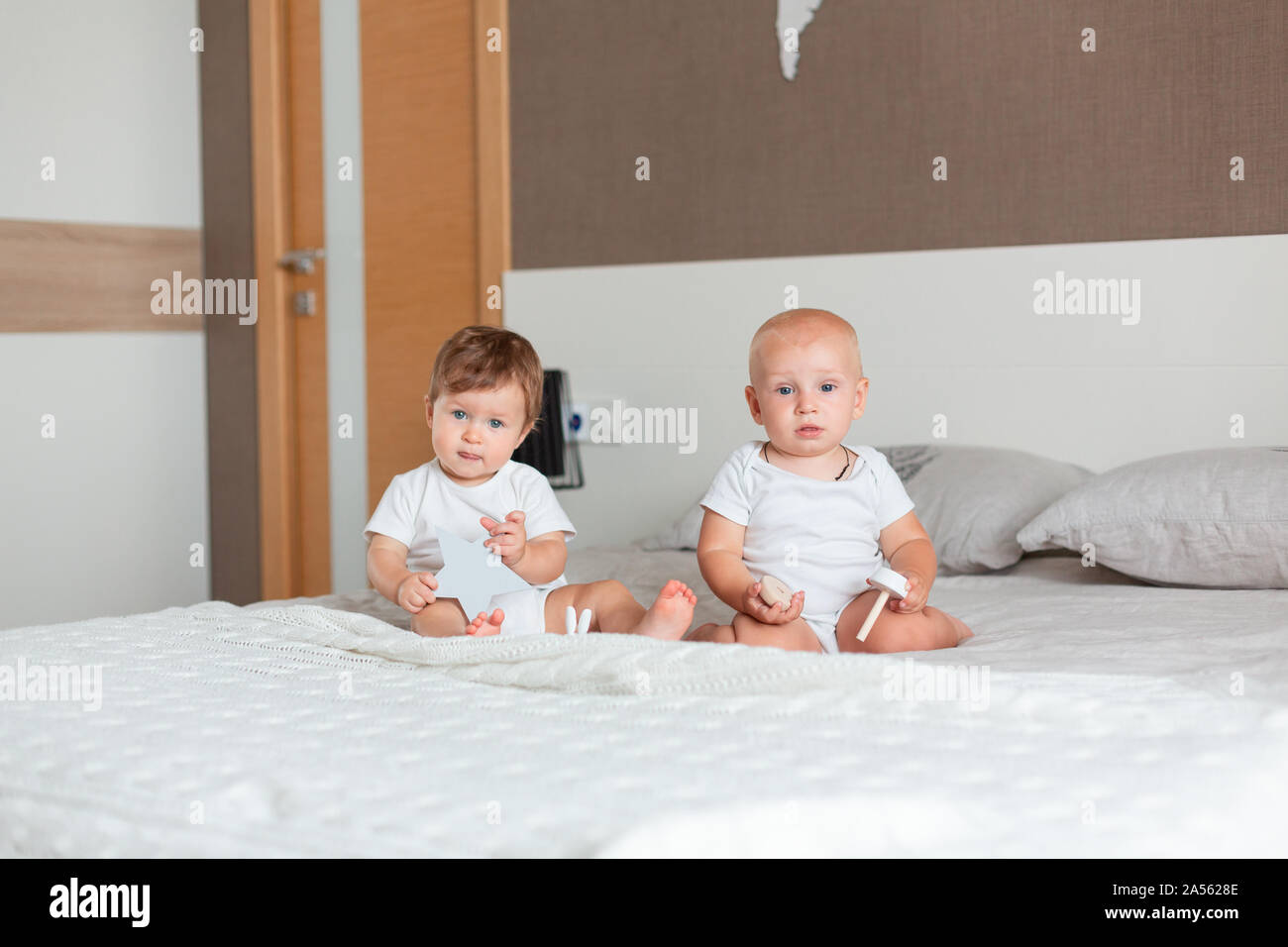 Due piccoli felici i bambini seduti su un letto matrimoniale in camera da letto Foto Stock