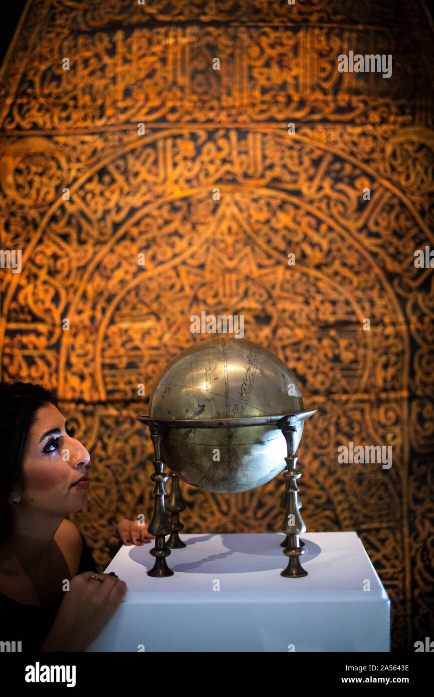 Un membro del personale guarda un ottone Safavid celestrial globe, realizzati in Persia nel XVII secolo (est. £80,000-120,000) davanti a un raro Maghribi gilt-filo di metallo cortina ricamata, realizzati in Nord Africa nel XVII secolo (est. £50,000-70,000) durante l'anteprima del Medio Oriente la settimana d'arte da Sotheby's a Londra, davanti a loro la vendita mediante asta pubblica il 22 e 23 ottobre. Foto di PA. Picture Data: venerdì 18 ottobre, 2019. Highlights della vendita includeranno una sontuosa foglia dal mitico 9th/decimo secolo Blue & Gold Corano, una pittura dinamica di una grande epica indiana corteo nuziale, gioielli compreso un Foto Stock