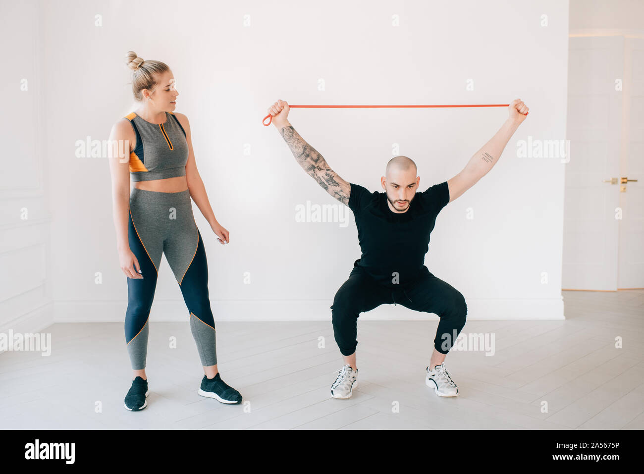 Donna osservando istruttore di fitness utilizzando la banda di resistenza in studio Foto Stock