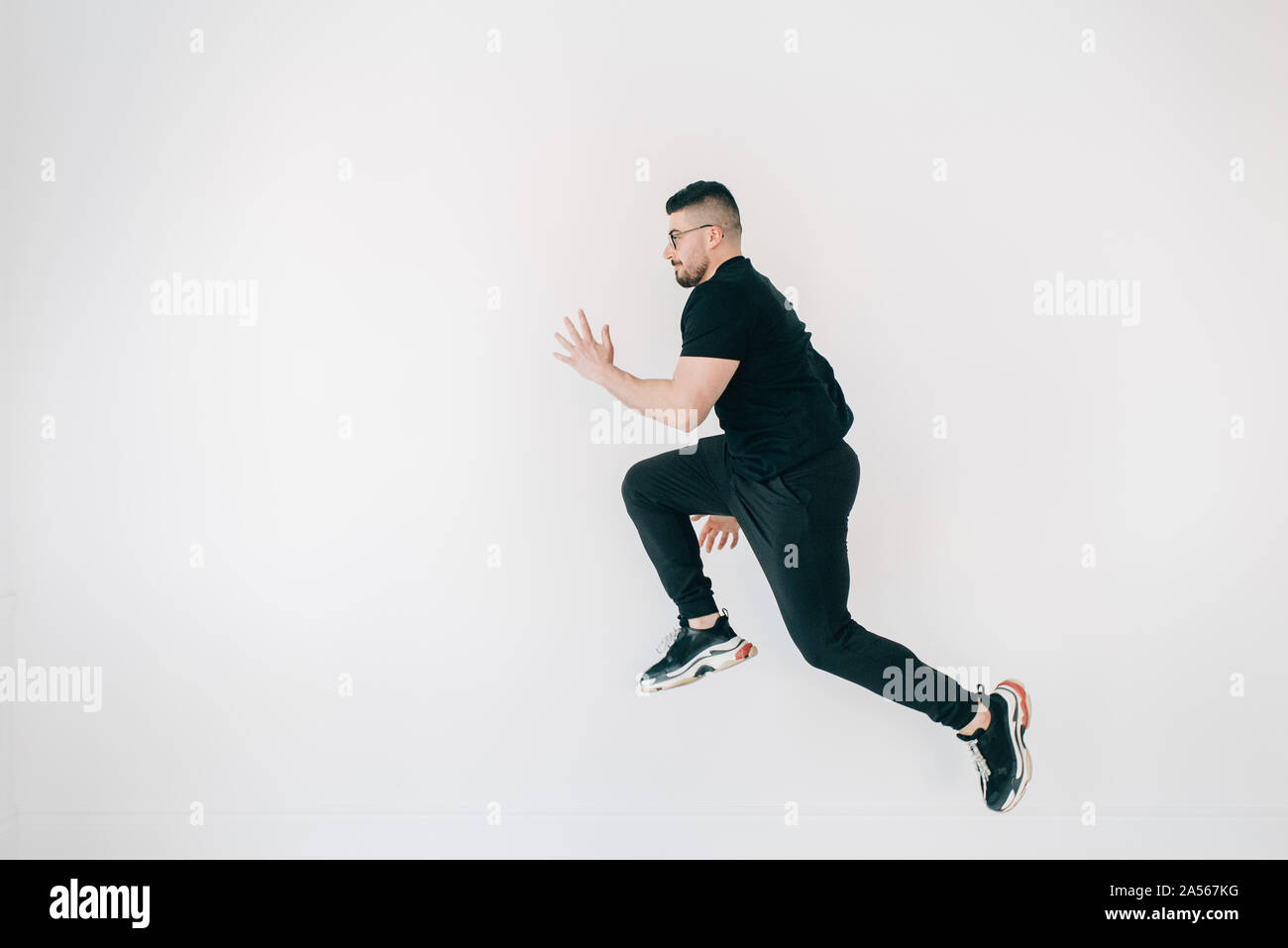 Uomo che fa del salto in alto contro il muro bianco Foto Stock