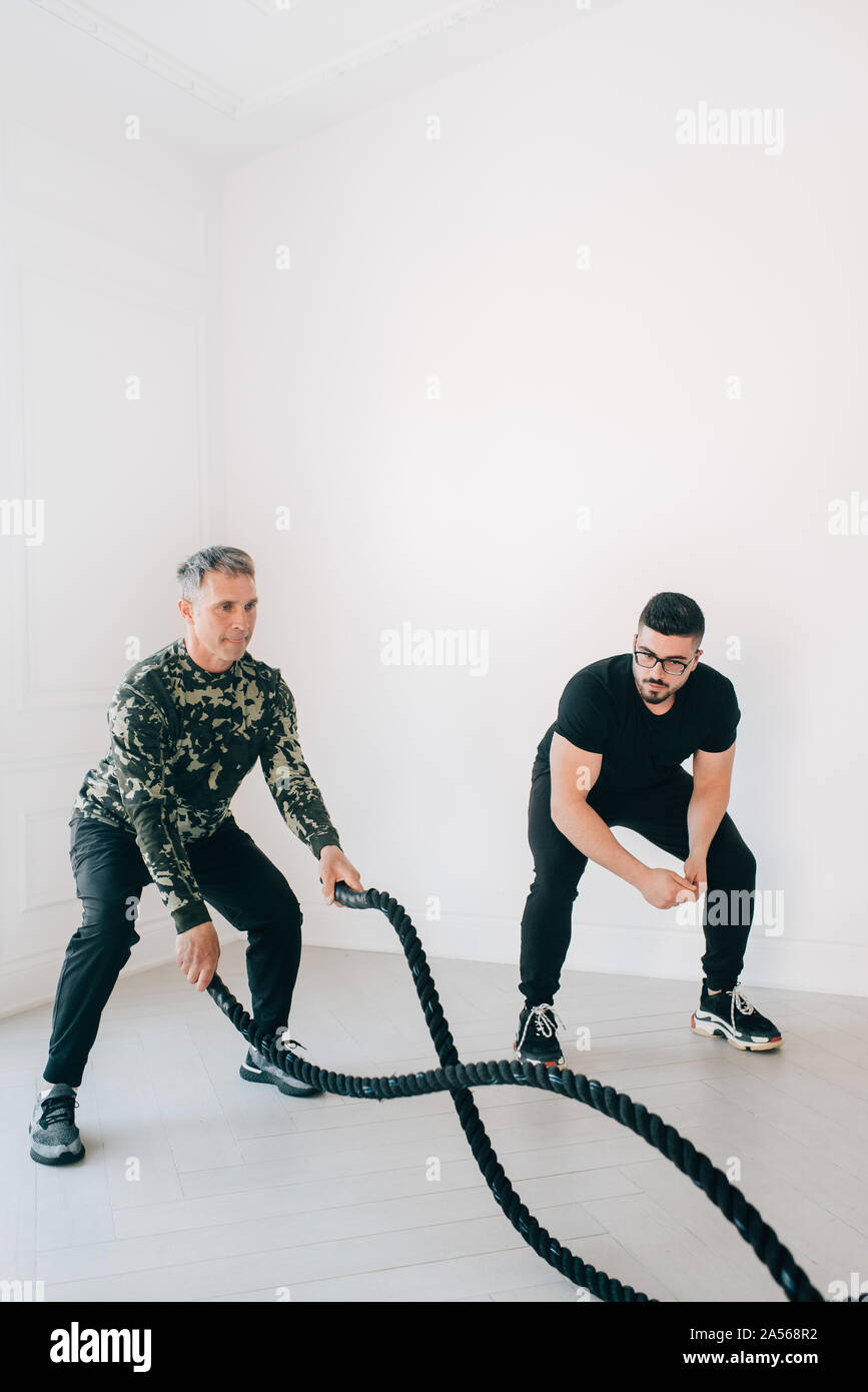 Istruttore di Fitness osservando l'uomo utilizzando la battaglia di corda in studio Foto Stock