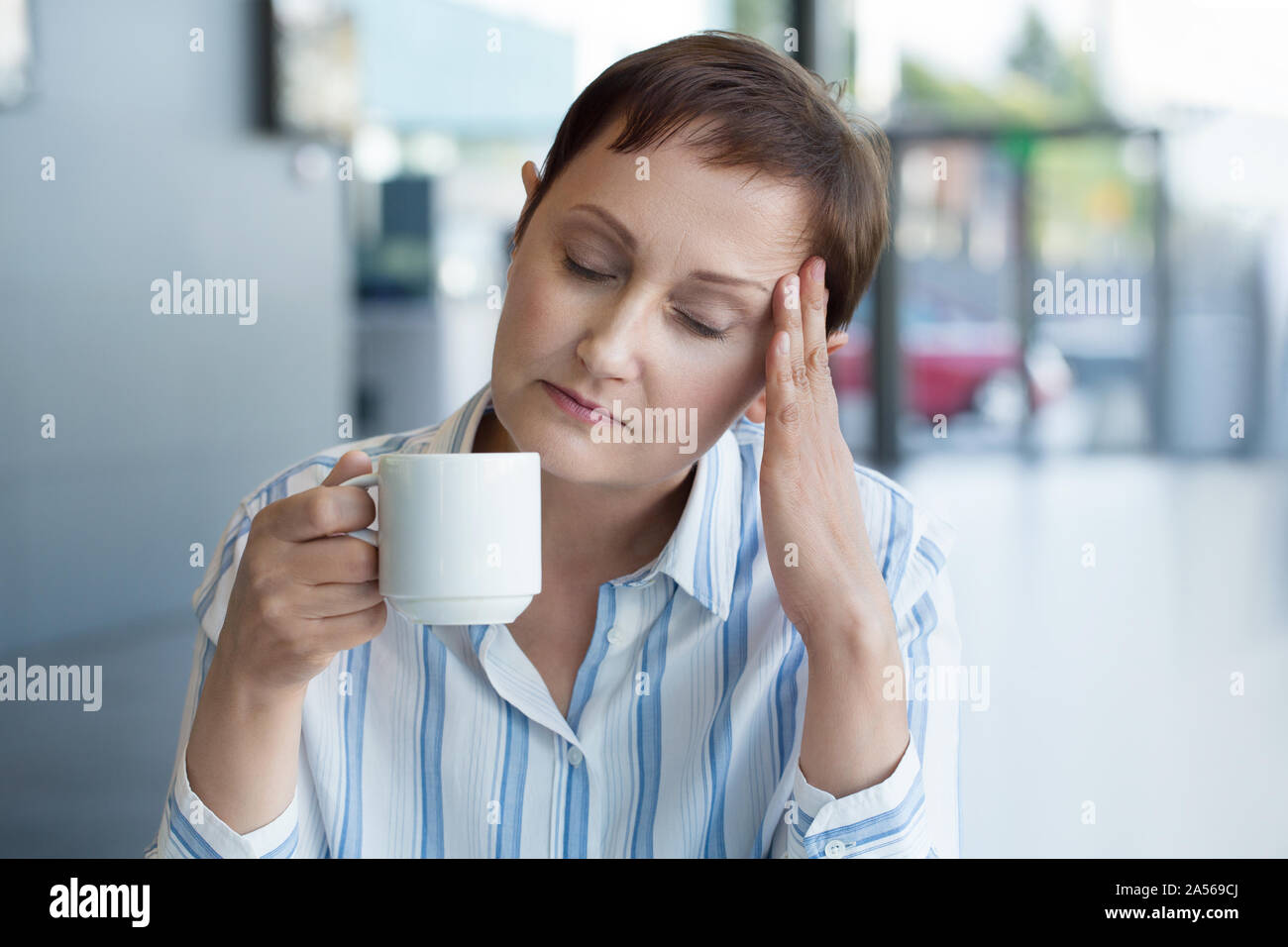 Business sentimento donna ha sottolineato dal lavoro in ufficio. Persone di mezza età femmina presentando un mal di testa e di bere il caffè o tè Foto Stock