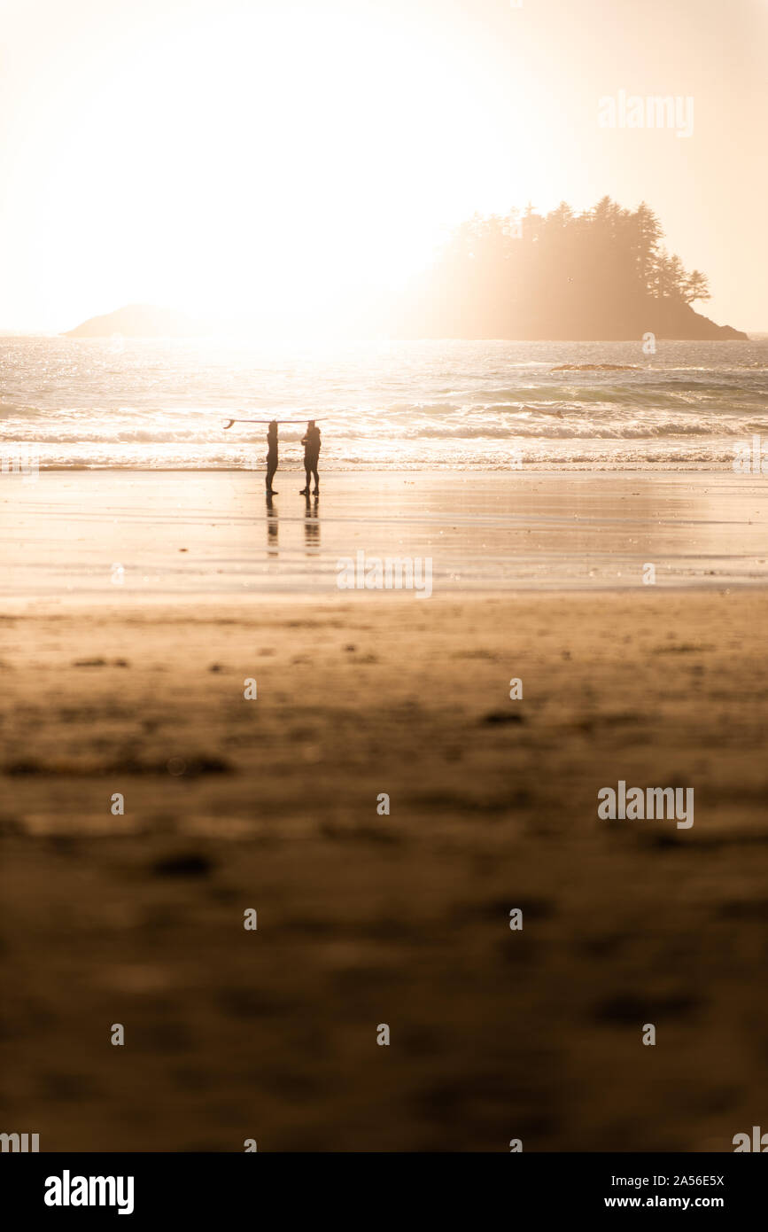Stagliano vista di due surfisti sulla spiaggia al tramonto, Tofino, Isola di Vancouver, Canada Foto Stock
