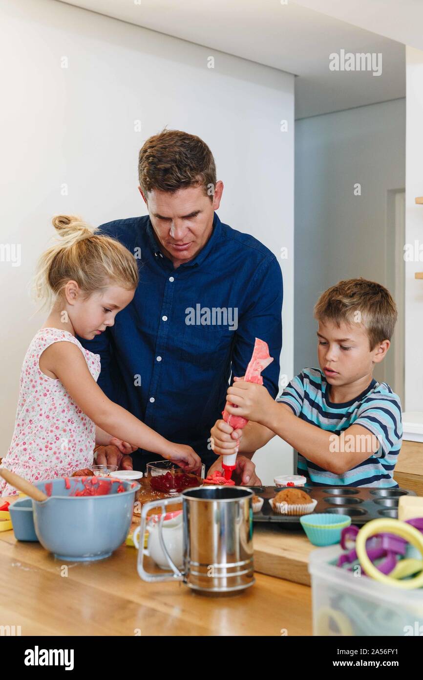 Padre e figli come decorare le tortine con la glassa in cucina Foto Stock