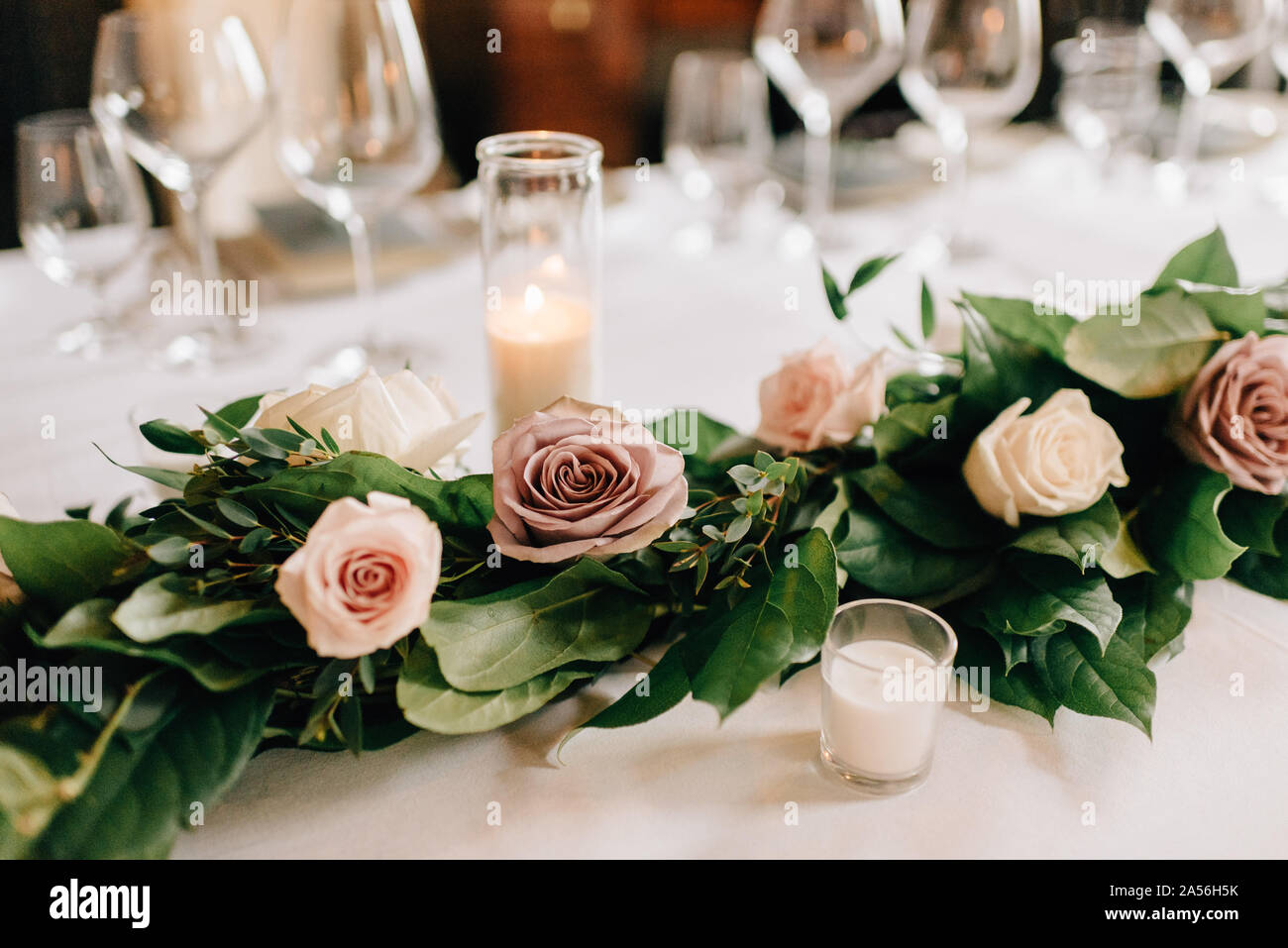 Posizionare l'impostazione al ricevimento di nozze tabella con rose garland decorazione, candele e bicchieri Foto Stock