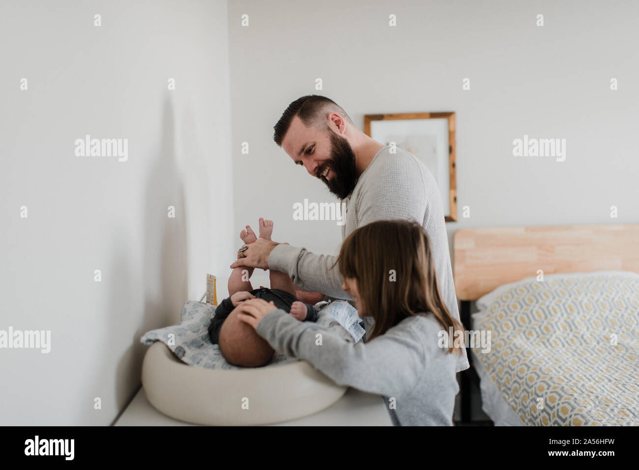 Il giovane e la figlia modifica baby figlio il pannolino in camera da letto, vista laterale Foto Stock