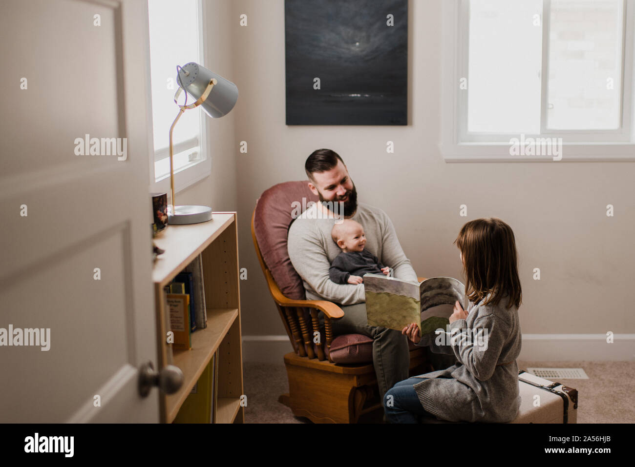 Ragazza nel soggiorno che mostra libro di padre e fratello di bambino Foto Stock