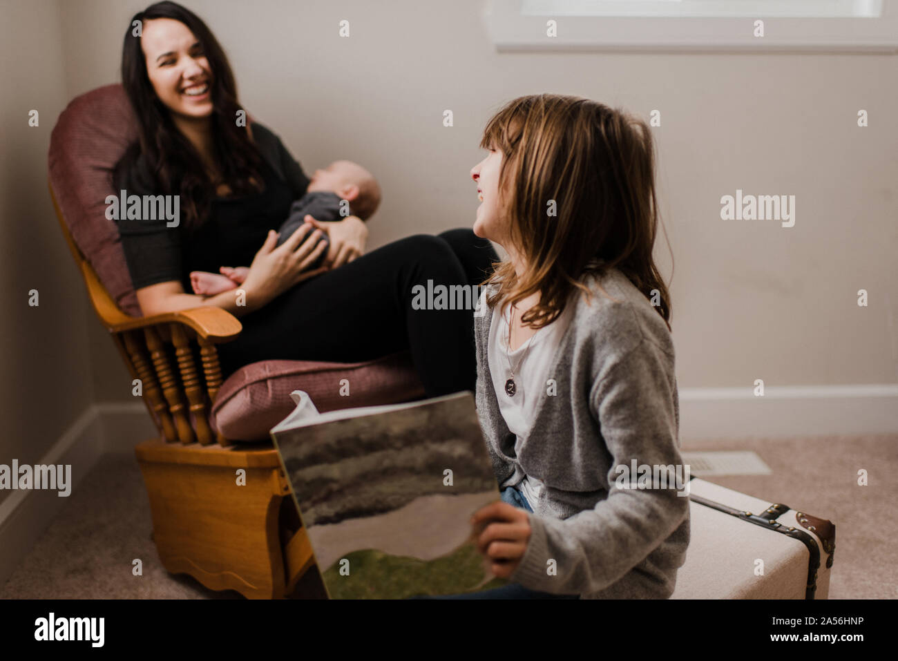 Ragazza ridere con la madre mentre ella culle baby fratello in salotto poltrona Foto Stock