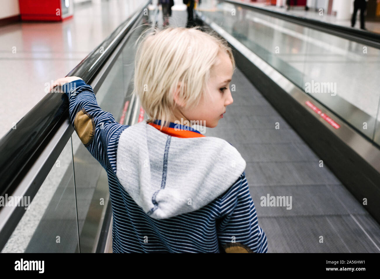 Capelli biondi boy su airport tapis roulant guardando sopra la sua spalla Foto Stock