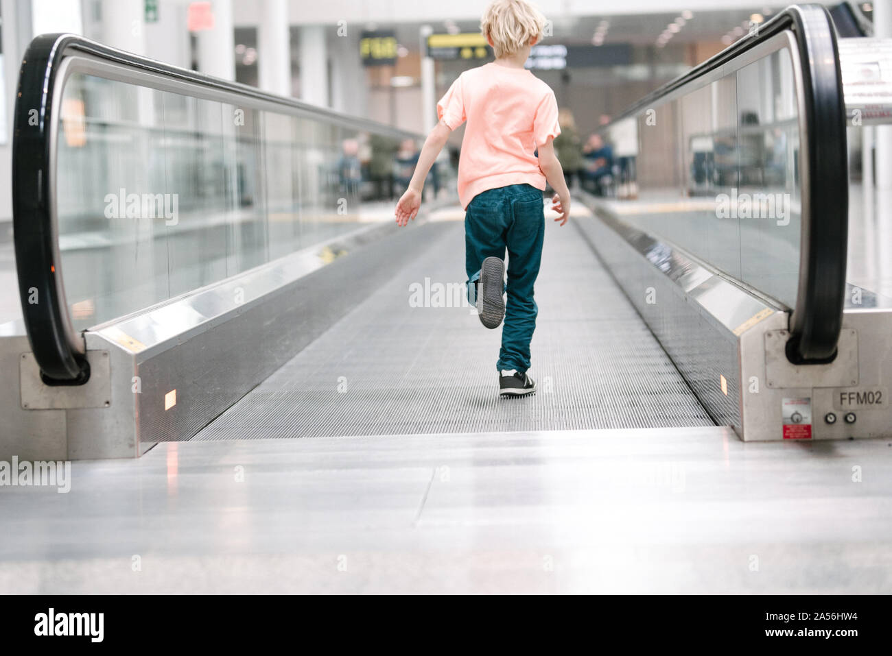 Ragazzo in esecuzione sul tapis roulant in aeroporto, a lunghezza piena vista posteriore Foto Stock