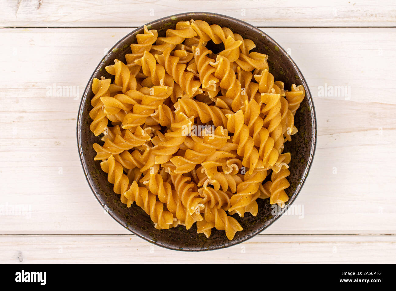 Sacco di tutto il marrone e secca fusilli integrali in ceramica scura flatlay ciotola in legno di colore bianco Foto Stock