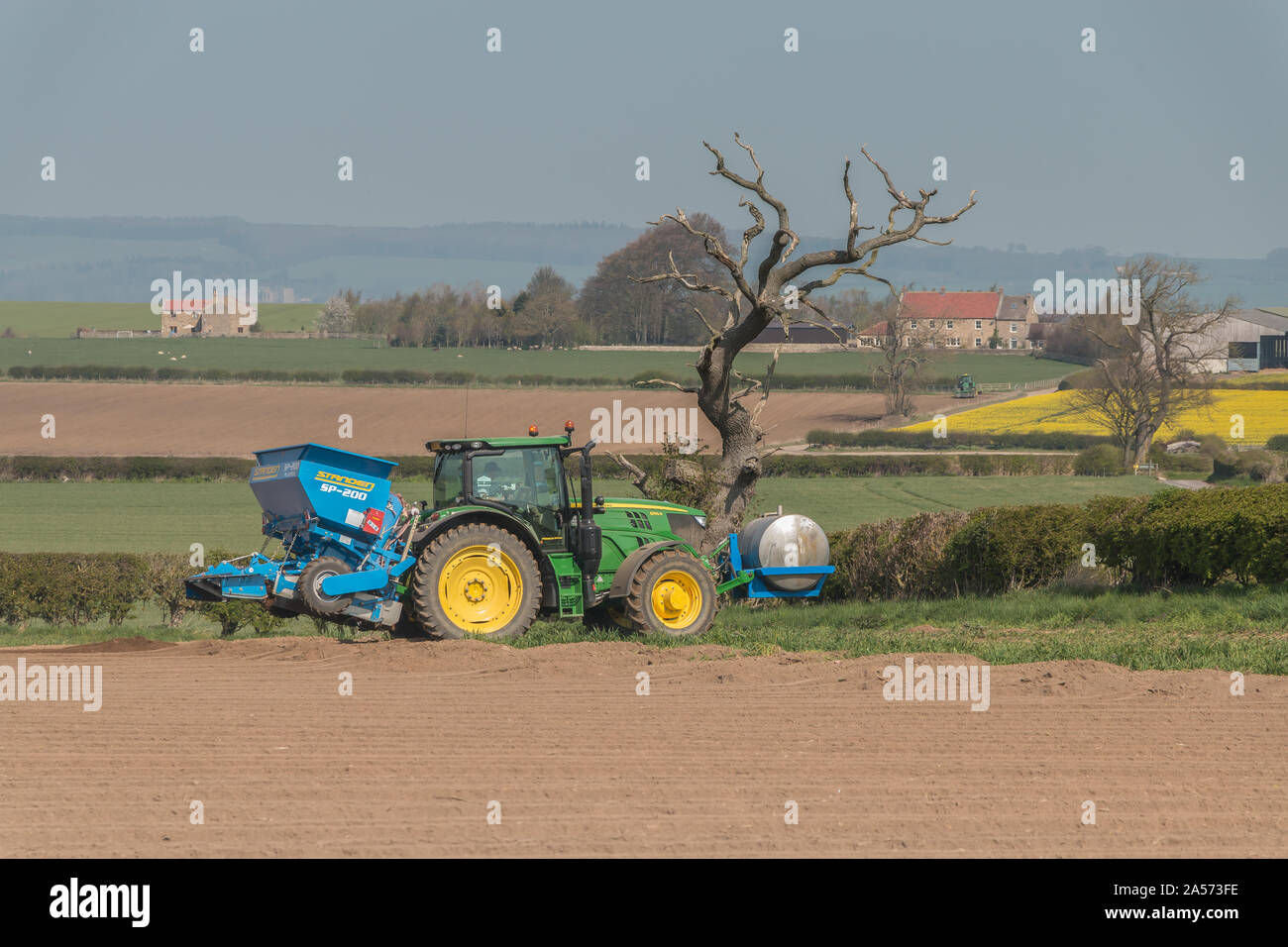 Un trattore John Deere e Standen piantatrice di patate a lavorare nel sole primaverile Foto Stock