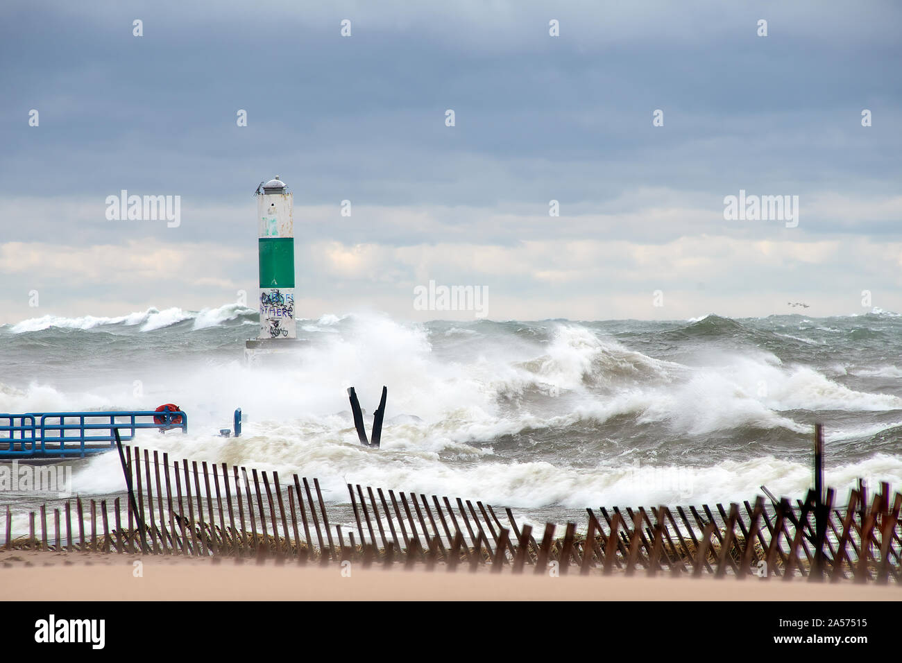 Alte onde tempestose sul Lago Michigan con verde e bianco marcatore di canale e recinzione in spiaggia Foto Stock