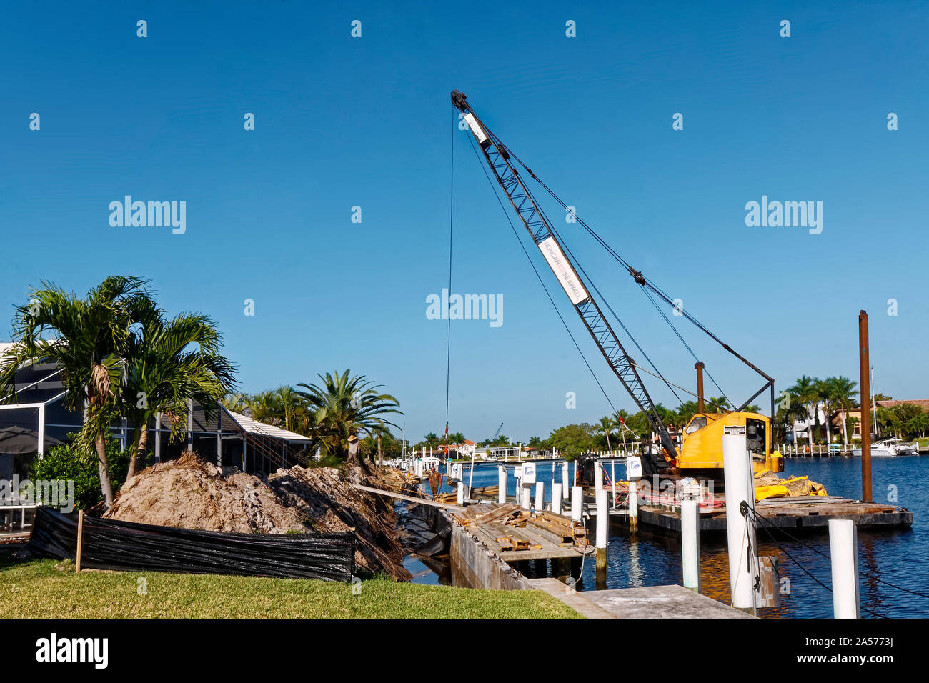 Riparazione di parete del mare; gru su chiatta; cumuli di sporcizia; docks; manutenzione; lavoro; lavoro; canal, case, Punta Gorda; FL; Florida; la molla; orizzontale Foto Stock
