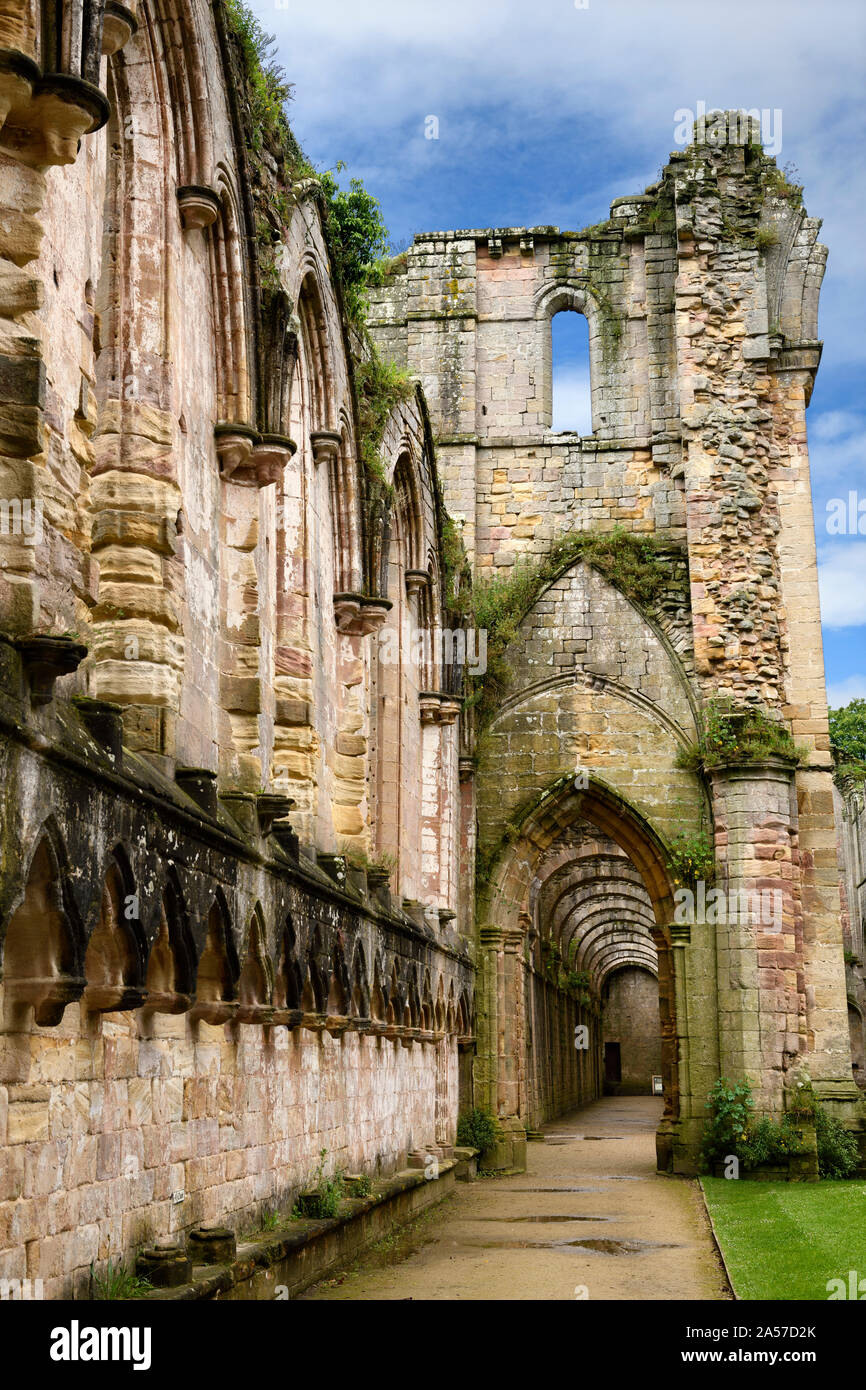 Con corridoio interno e bagnato pietra erosa archi presso la navata di Fountains Abbey monastero cistercense rovine della chiesa nello Yorkshire del Nord Inghilterra Foto Stock