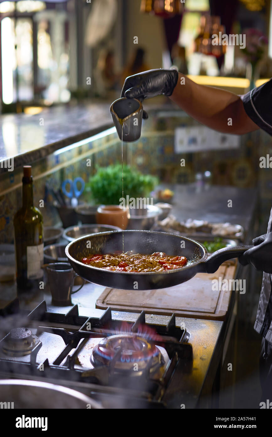 Concetto di cibo. Lo chef aggiunge le spezie friggere in una padella i pomodori e le ostriche. Il processo di cottura di spaghetti con frutti di mare. Foto Stock