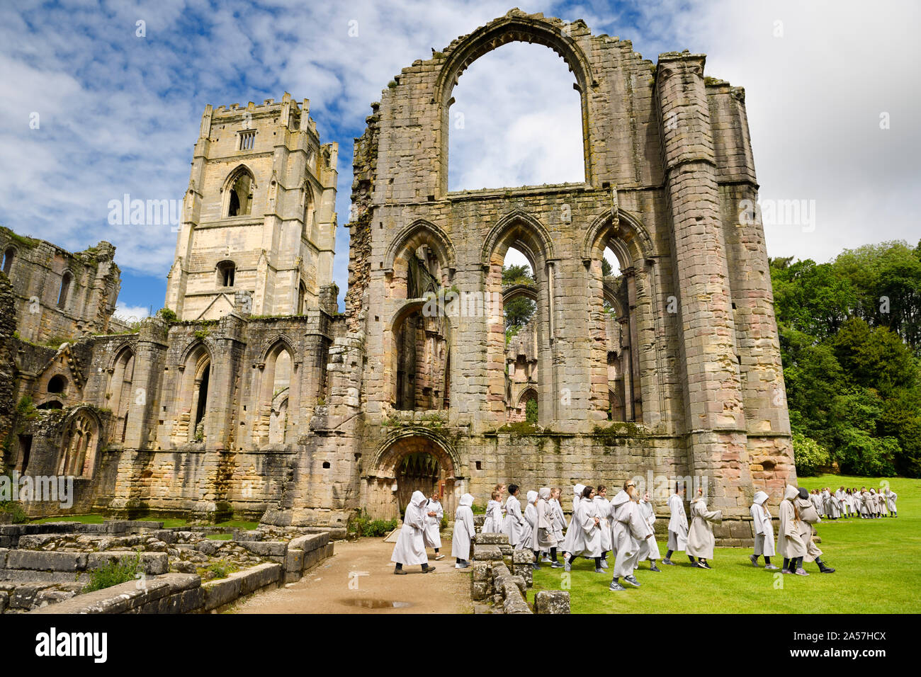 Fountains Abbey monastero cistercense chiesa con torre e Cappella di altari e di un gruppo di studenti di monaco accappatoi North Yorkshire, Inghilterra Foto Stock