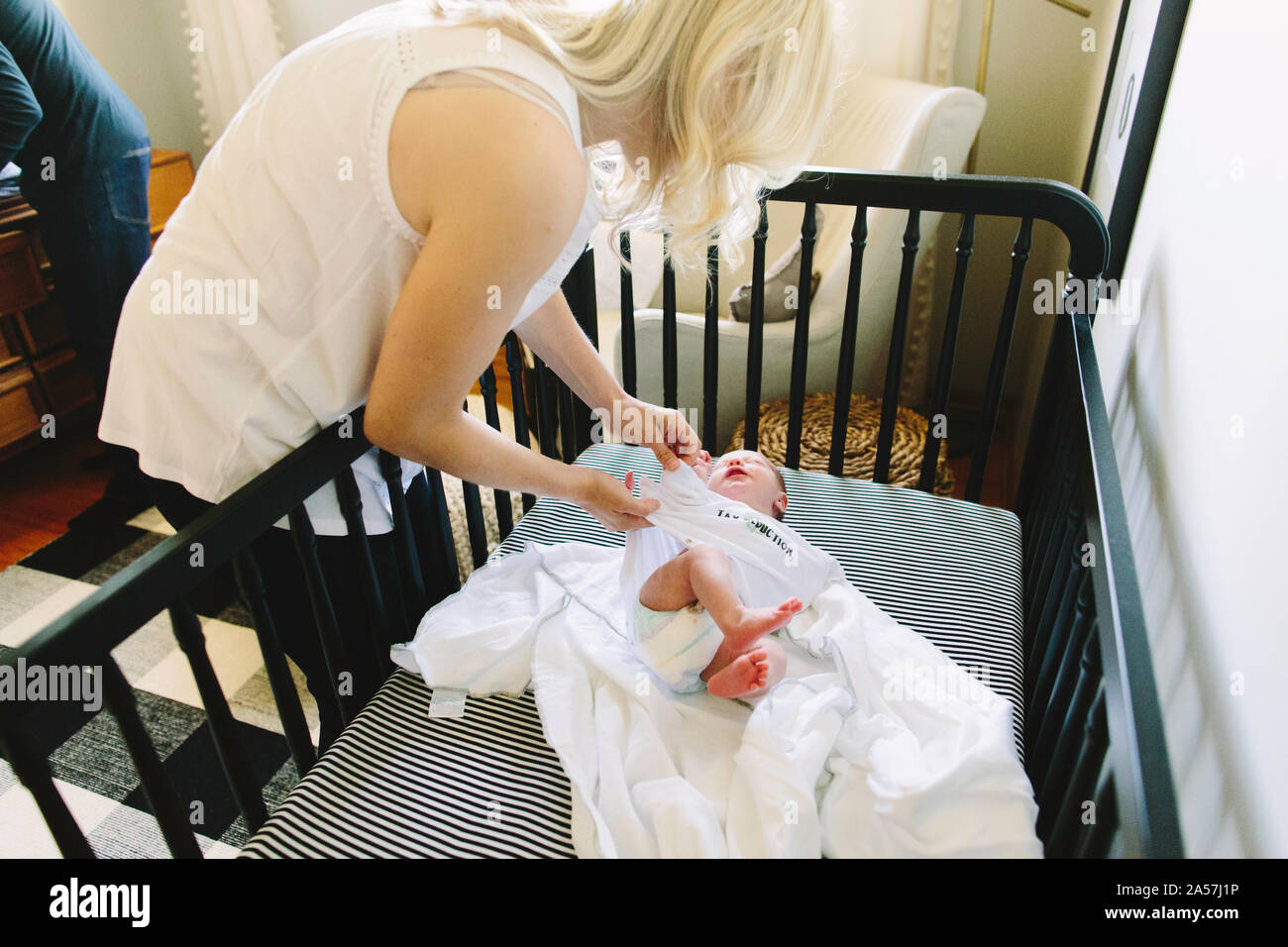 Una mamma regolare il suo neonato vestiti mentre egli stabilisce in una culla Foto Stock