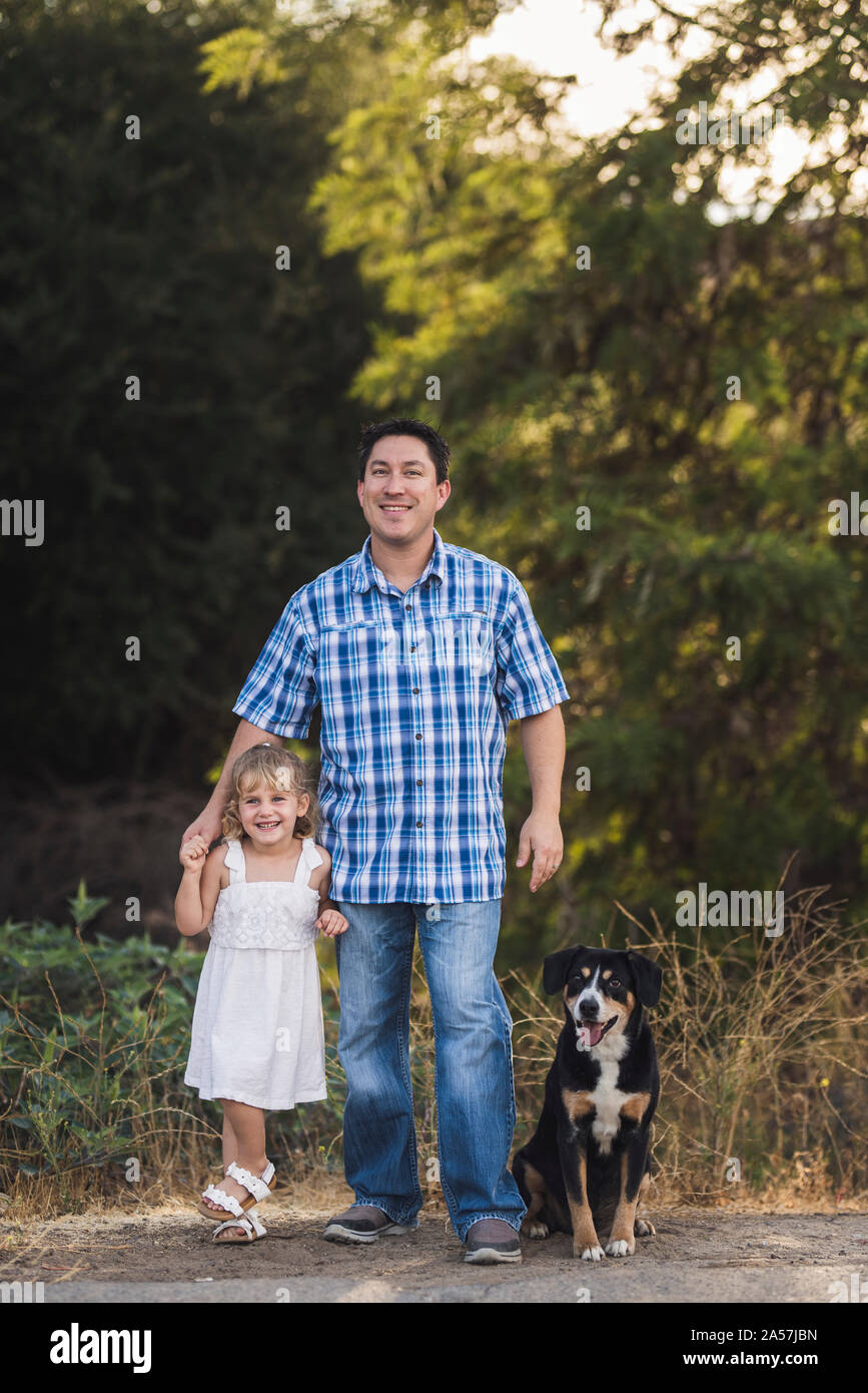 Papà sorridente all aperto con adorabile figlia giovane e felice cane Foto Stock