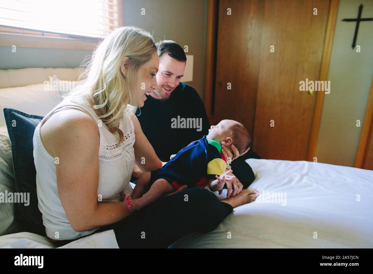 Una mamma e papà interagiscono con il loro figlio neonato mentre è seduto su un letto Foto Stock