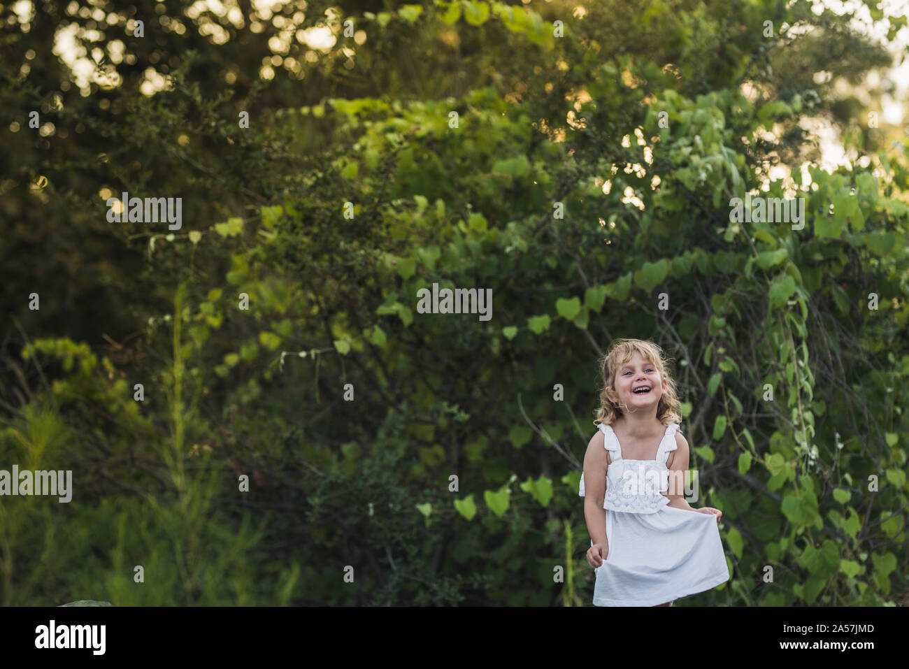 Ridendo giovane ragazza in abito bianco con sfondo del fitto fogliame Foto Stock