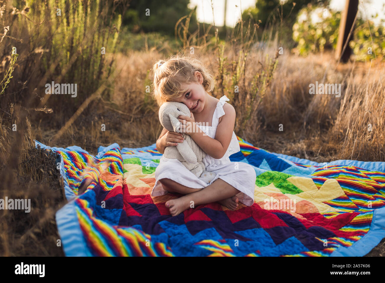 A piedi nudi 4 yr old girl snuggling peluche sul bold piumini colorati Foto Stock