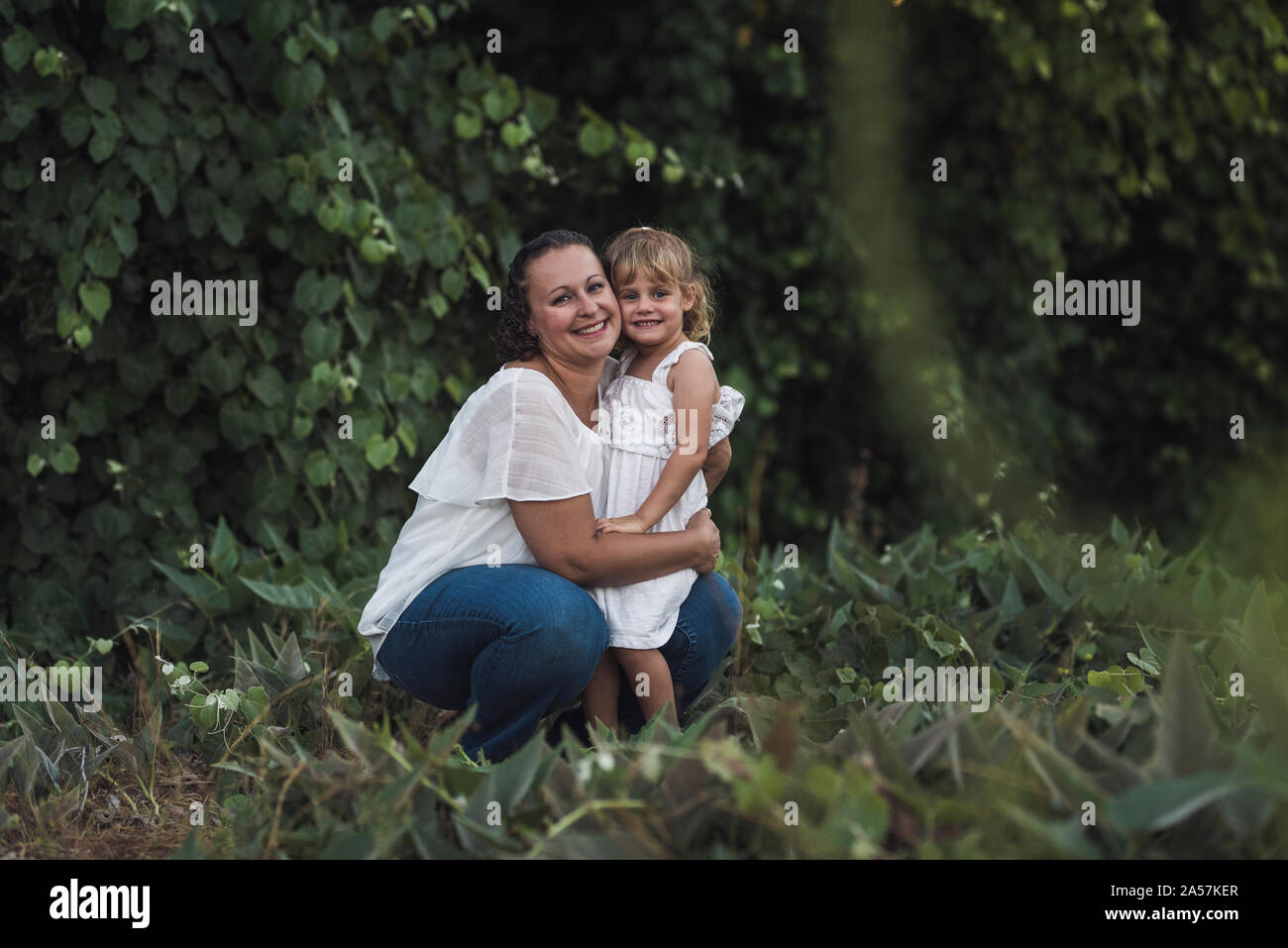 Inginocchiato mom abbracciando felice figlia all'aperto nelle vicinanze del Tree Foto Stock