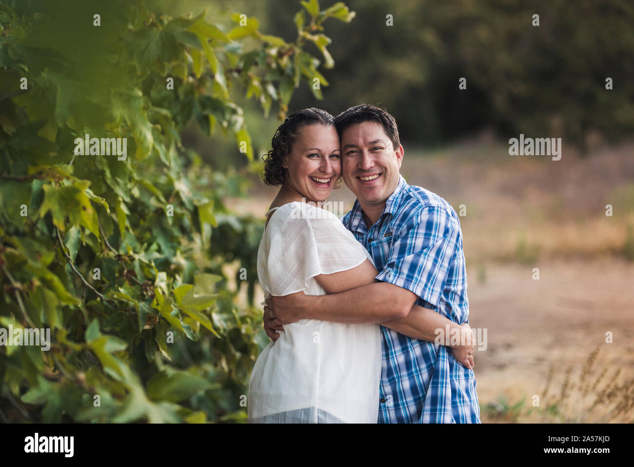 Sorridente marito e moglie abbracciando sotto foglie vininggreen Foto Stock