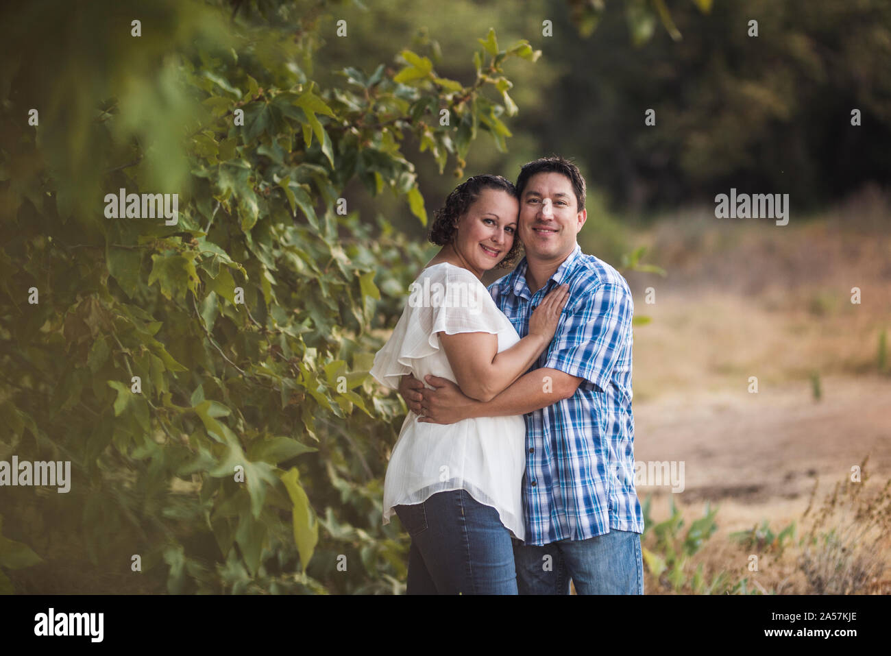 Sorridente marito e moglie abbracciando in prato vicino a fogliame verde Foto Stock