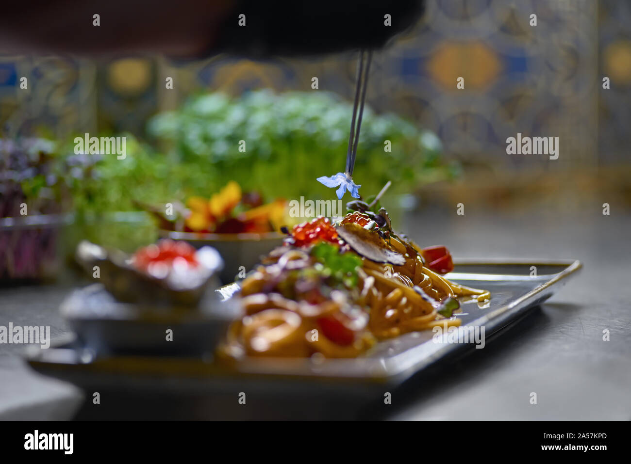 Concetto di cibo. Lo chef è decorata con erbe aromatiche e fiori piatti nel ristorante. Il processo per la fabbricazione di spaghetti con frutti di mare. Foto Stock