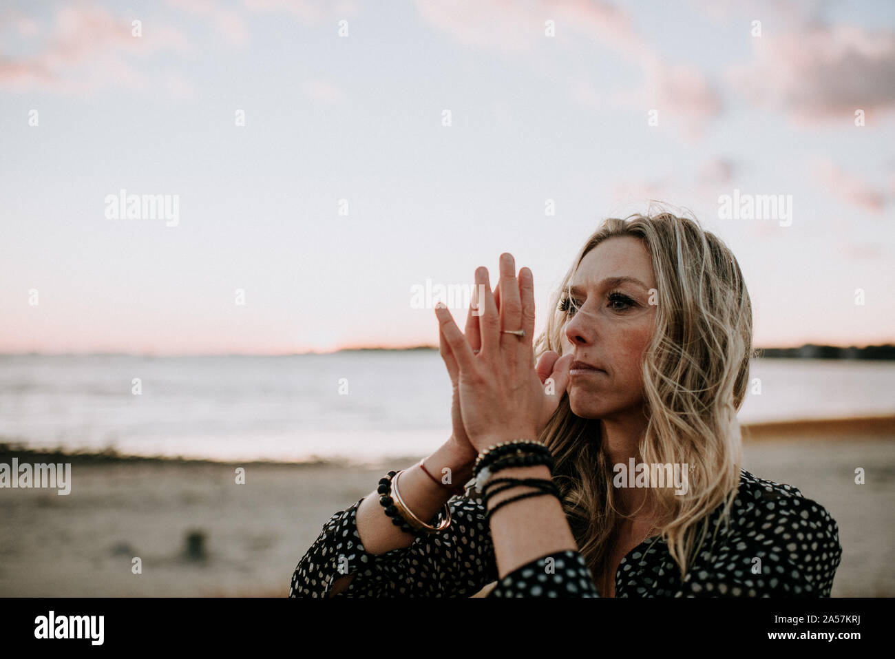 Donna con la preghiera le mani sulla spiaggia al tramonto Foto Stock