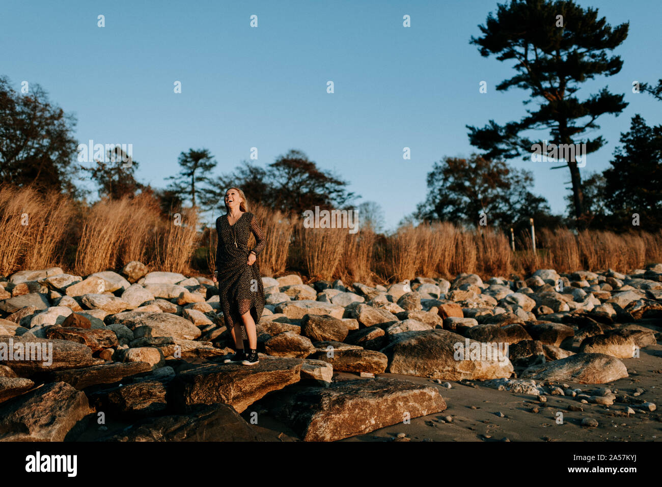 Donna su rocce sulla spiaggia al tramonto Foto Stock