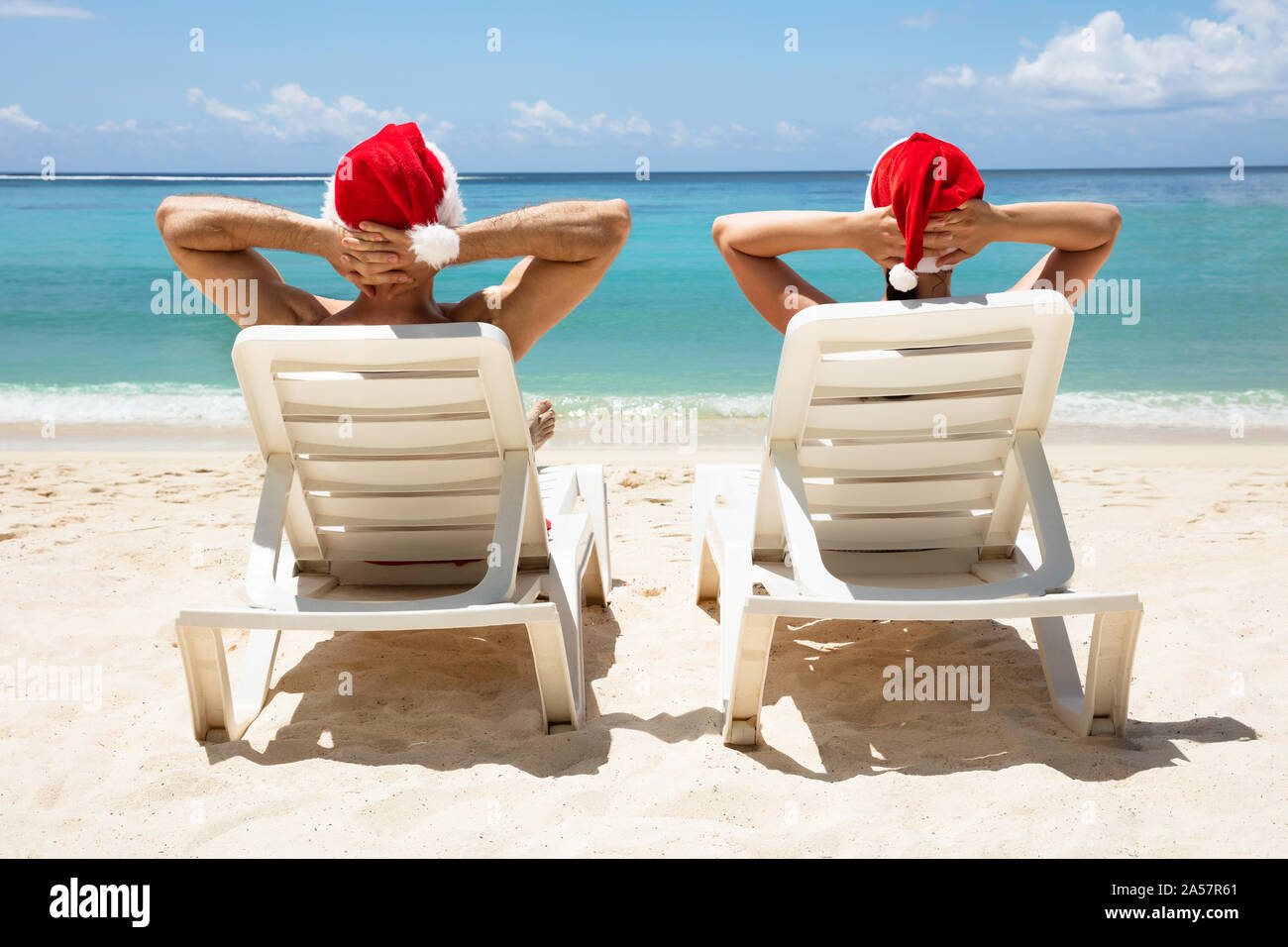 Vista posteriore di un paio di indossare cappelli di Babbo Natale rilassante su bianco Sedie a sdraio sulla spiaggia Foto Stock