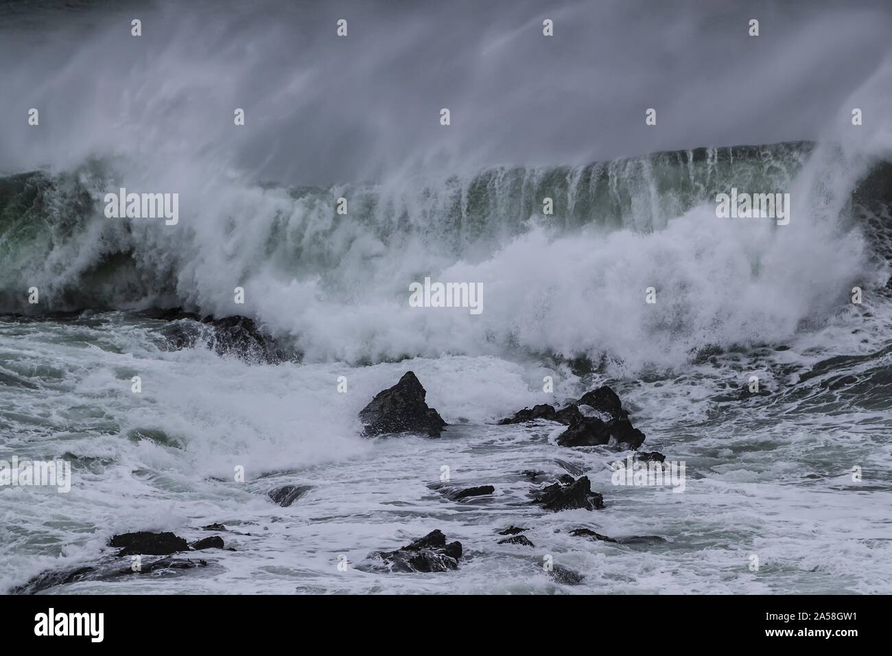 Forte onda che arriva e spruzzi alle pietre nell'onda 'Cribber', Newquay, Cornovaglia, Regno Unito Foto Stock