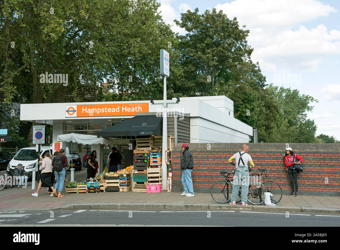 Persone tra ciclista e frutta in stallo al di fuori di Hampstead Heath Overground Stazione, estremità Sud verde, London Borough of Camden Foto Stock