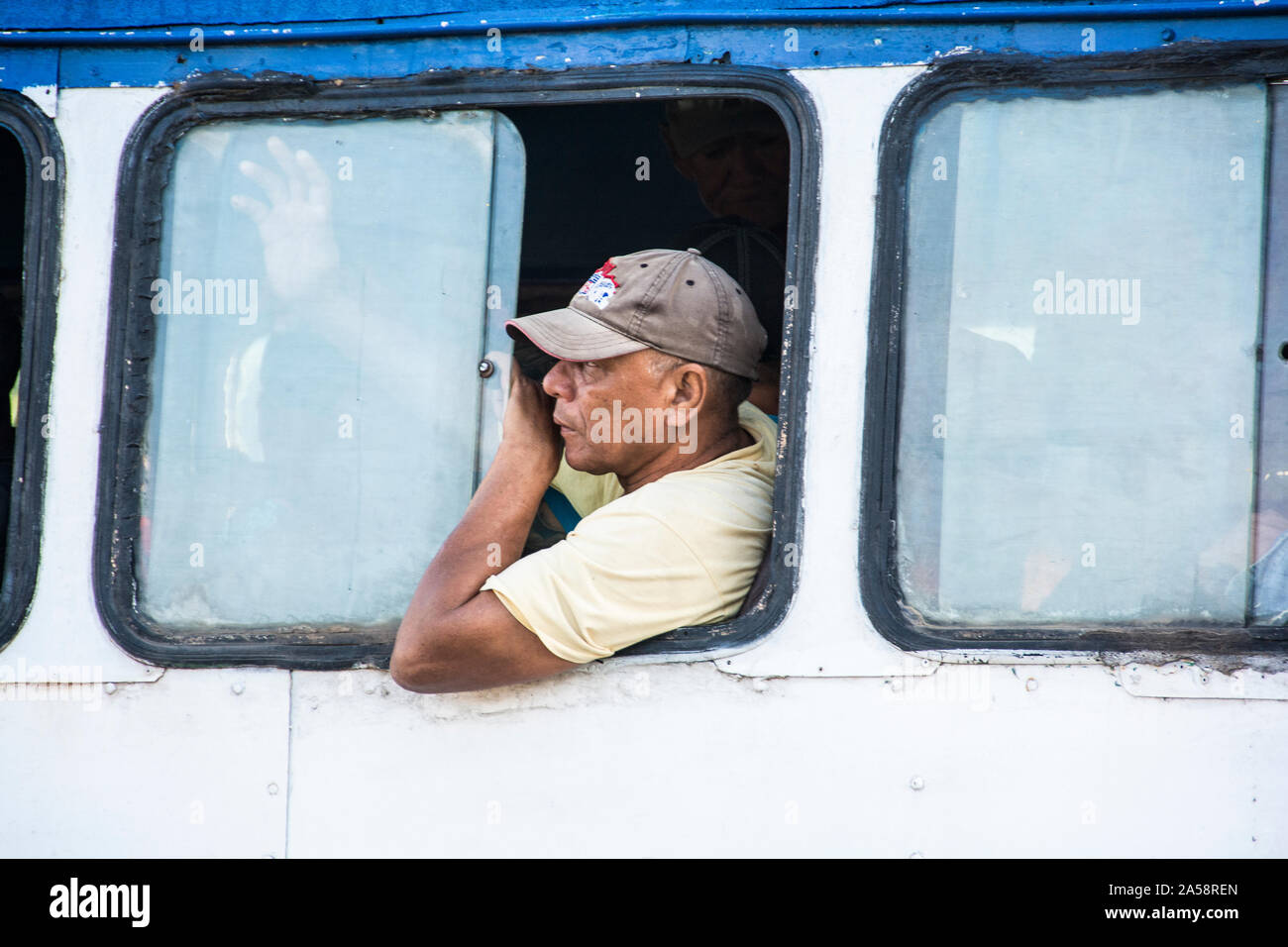 Un uomo cubano nei suoi anni 50, con un cappuccio, a cavallo dell'autobus; Camaguey, Cuba Foto Stock