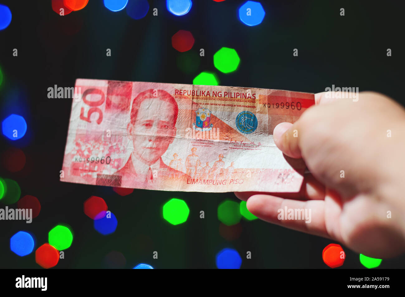 Immagine ravvicinata di una mano che tiene o distribuendo un filippino cinquanta pesos in contanti durante vacanze di Natale. Foto Stock