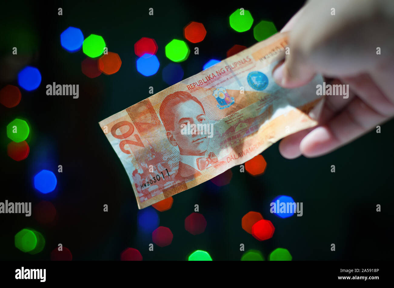 Immagine ravvicinata di una mano che tiene o distribuendo un filippino venti pesos in contanti durante vacanze di Natale. Foto Stock