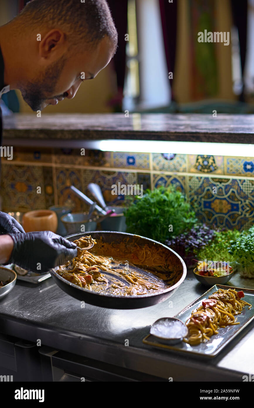 Concetto di cibo. Lo chef mescola gli spaghetti al dente in una padella i pomodori e le ostriche, piatto in un ristorante. Il processo di cottura di spaghetti con frutti di mare. Foto Stock
