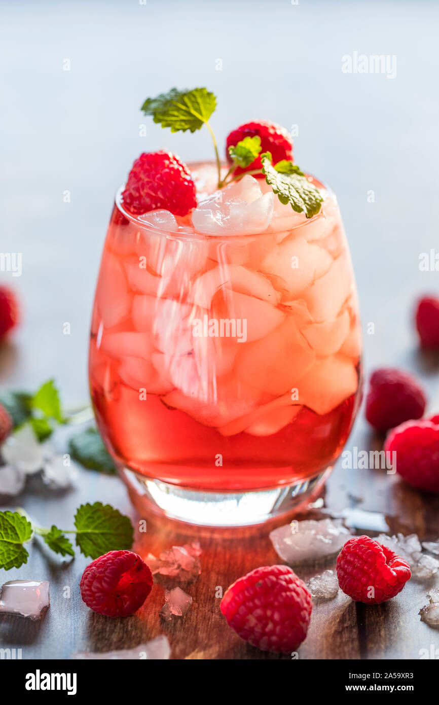 Close-up di un rosso rinfrescanti drink traslucido con ghiaccio e lamponi. Il succo è guarnito con una foglia verde e therer sono pezzi di ghiaccio e Foto Stock