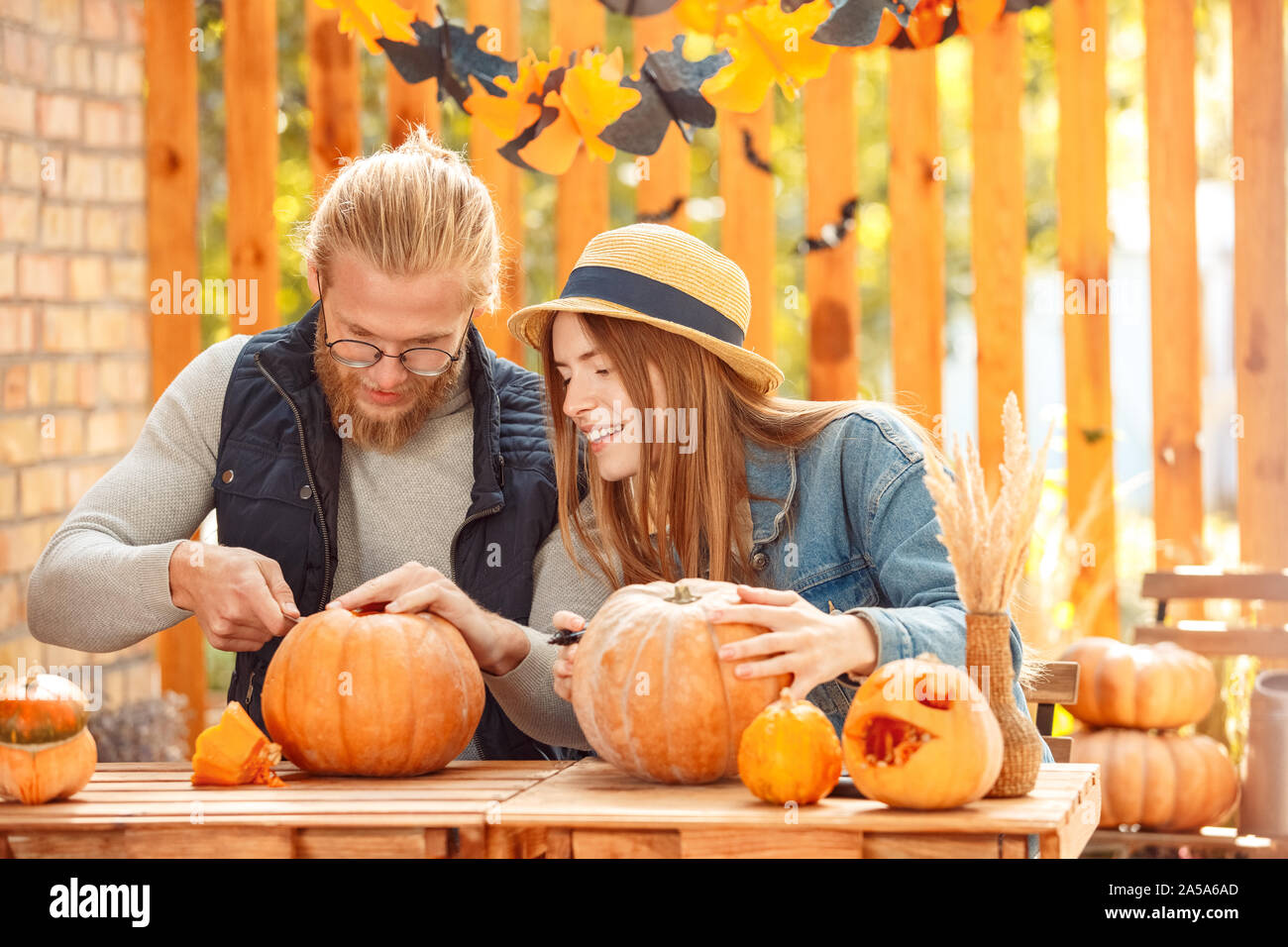 Halloween Preparaton concetto. Coppia giovane seduto a tavola all'esterno rendendo jack-o-lantern sorridente allegro Foto Stock