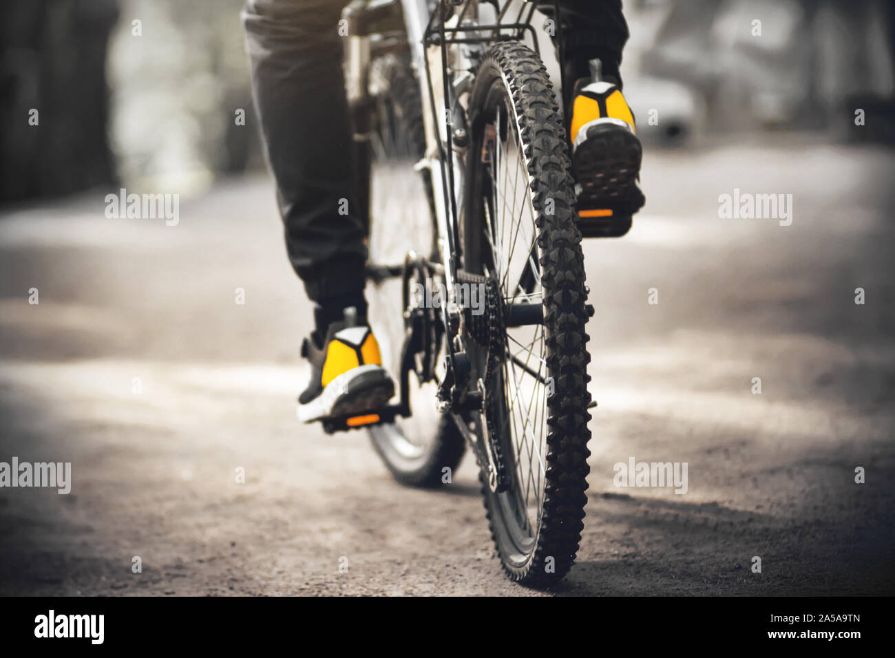 Un uomo sportivo in giallo sneakers cavalca un nero delle moto sportive con pedali con catarifrangenti arancioni su una strada di sabbia illuminata dalla luce del sole. Foto Stock